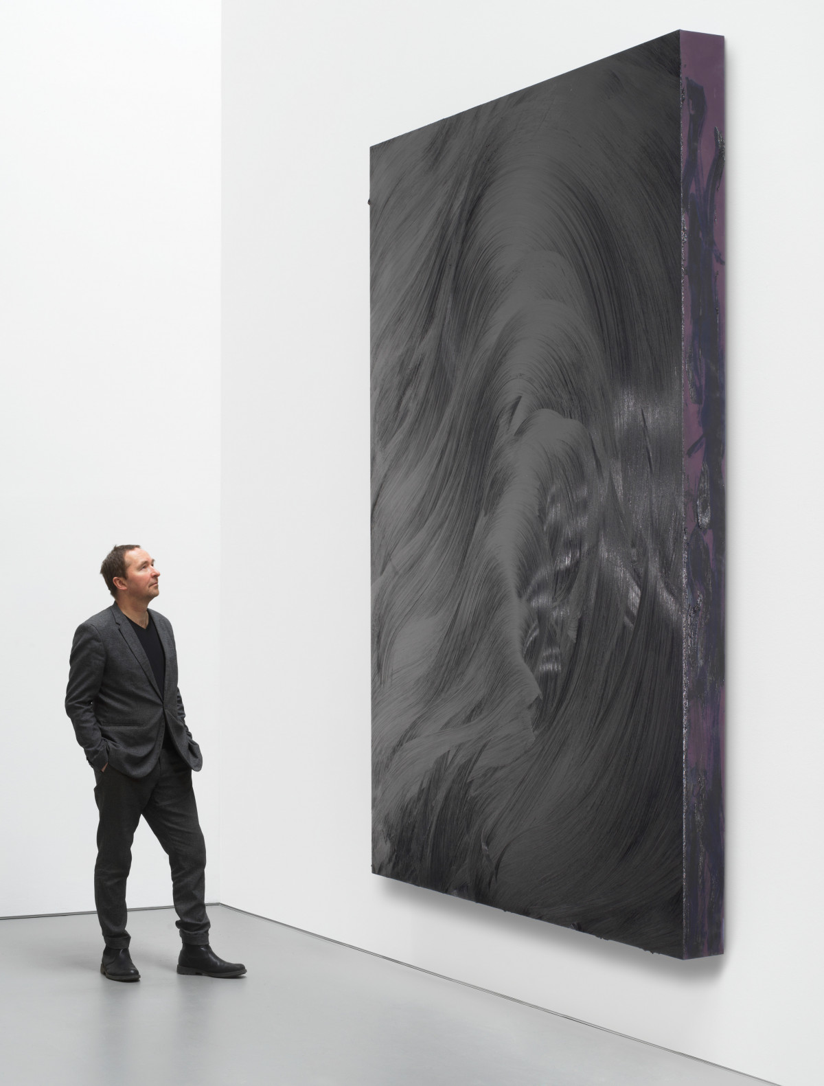 A large black painting by the british artist with a person standing next to it.